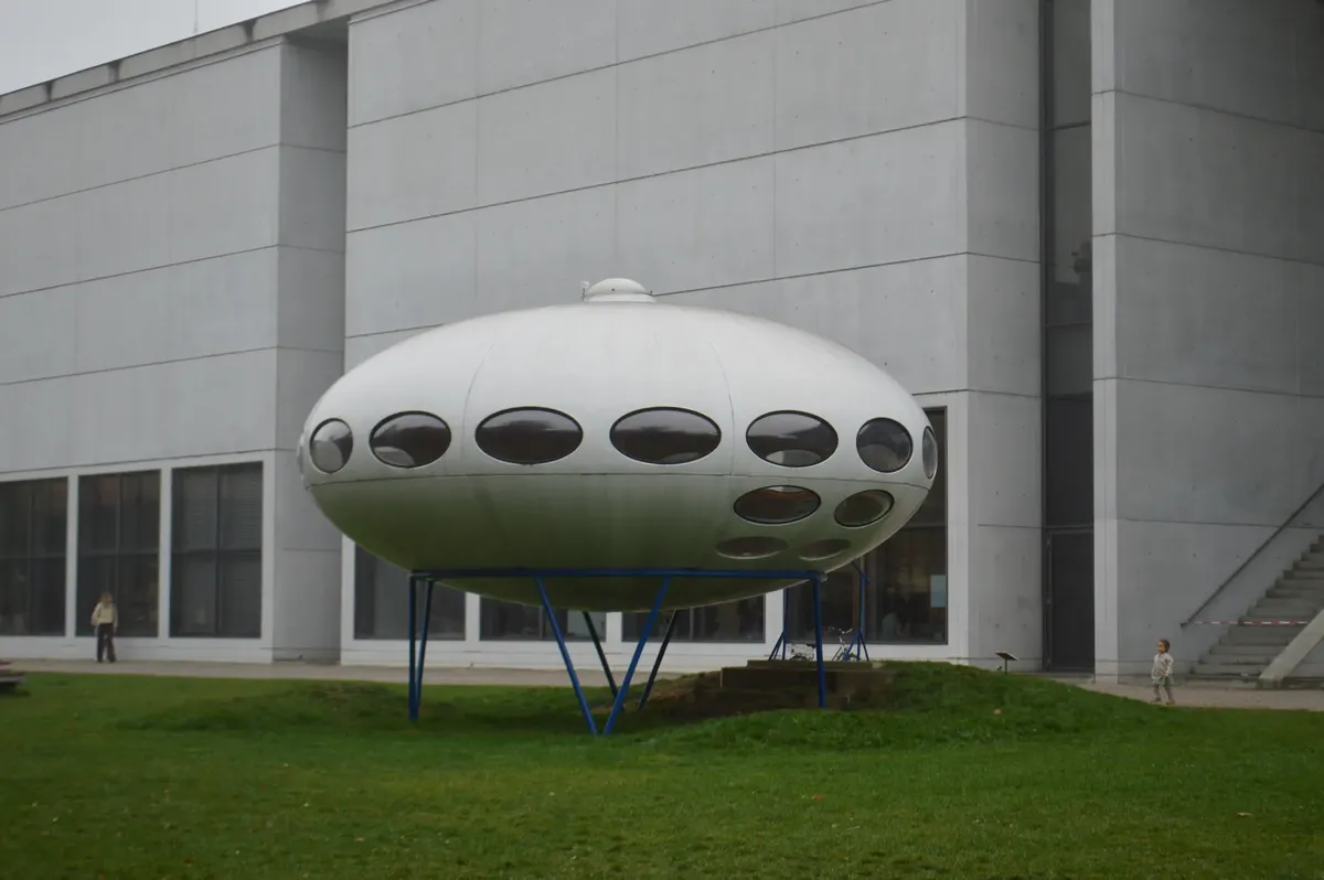 Modern UFO-like structure outside a contemporary building on a foggy day.