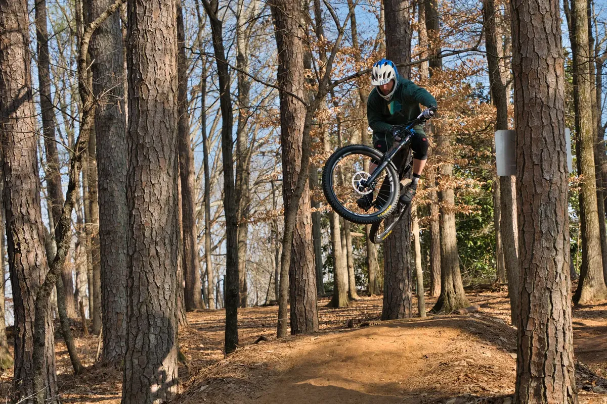 Thrilling action shot of a mountain biker mid-air in a dense forest setting in Roswell, GA.